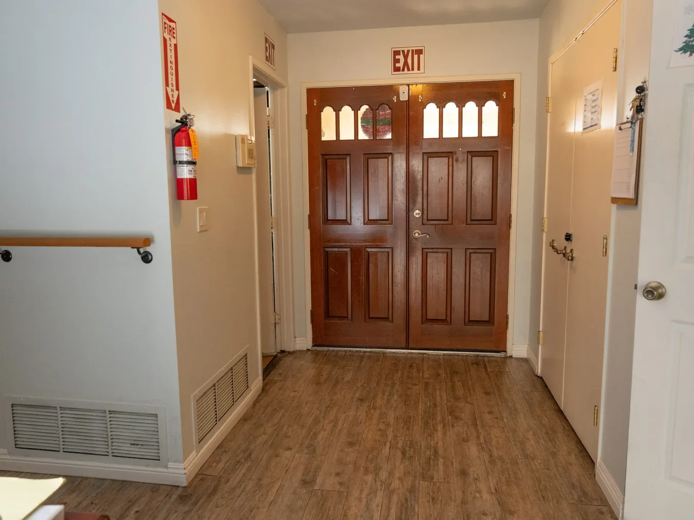 Accessible hallway with safety features including handrail, fire extinguisher, and clearly marked exit doors in residential care facility