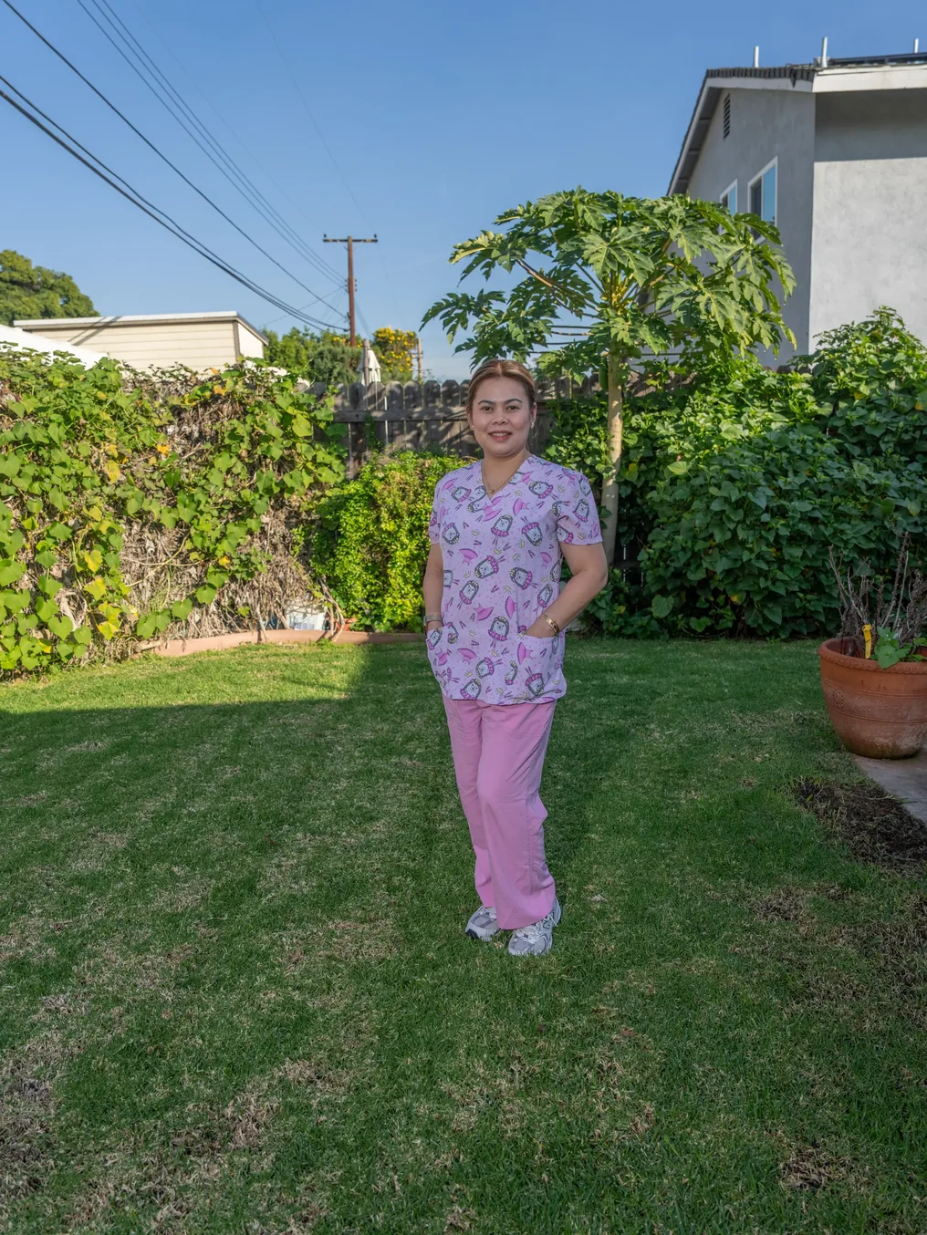Professional caregiver in patterned scrubs standing in sunny residential garden setting