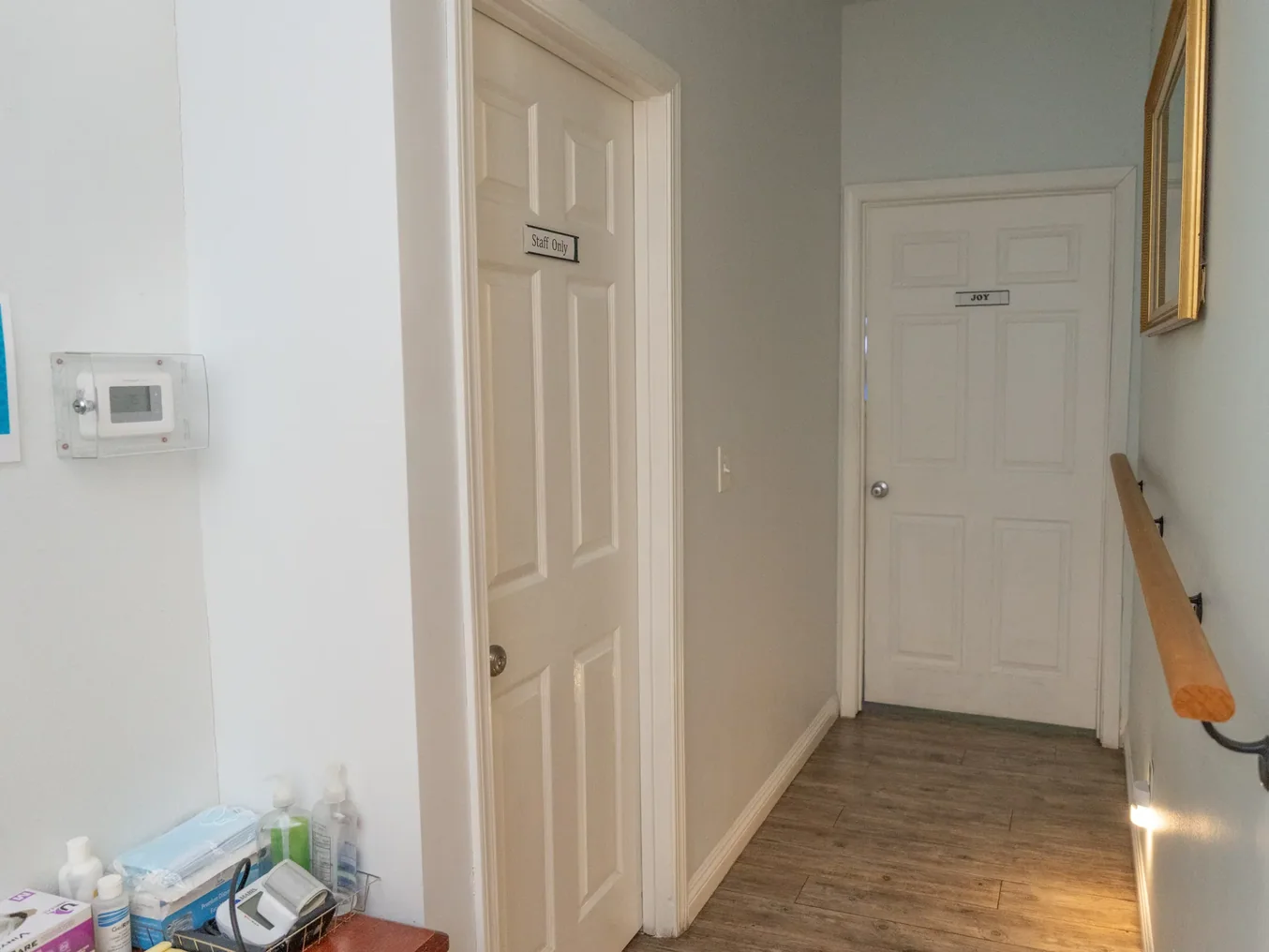 Clean hallway in care facility with accessible handrail and clearly labeled staff and resident room doors